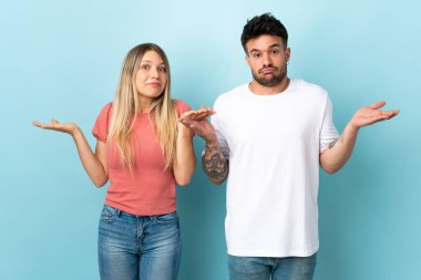Kafkasyalı genç bir çift mavi arka planda izole edilmiş. Şüpheleri var ve kafası karışmış bir yüz ifadesi var.