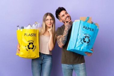 Kafkasyalı genç çift, mor arka planda izole edilmiş bir şekilde geri dönüşüm yaparken yukarı bakarken bir fikir üretiyor.