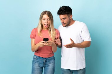 Mavi arka planda izole edilmiş genç beyaz çift cep telefonuyla mesaj ya da e-posta gönderiyor.