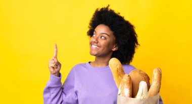 Genç Afrikalı Amerikalı bir kadın sarı arka planda izole edilmiş bir ekmek alıyor.