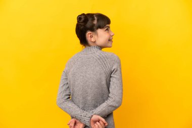 Küçük beyaz kız sarı arka planda izole edilmiş ve arkasına bakıyor.