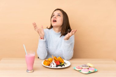 Bej arka planda izole edilmiş waffle yiyen genç kız kötü bir durum yüzünden hayal kırıklığına uğradı.
