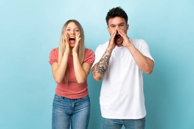 Mavi arka planda izole edilmiş genç beyaz çift ağızları açık bağırıyor.