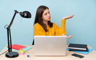 Öğrenci kız evinde çalışıyor. Mavi arka planda tek başına. Davet edilmek için ellerini yana uzatıyor.