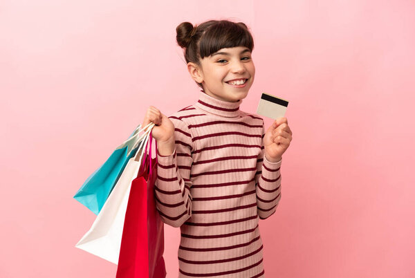 Маленькая белая девочка, изолированная на розовом фоне, держащая сумки с покупками и кредитку