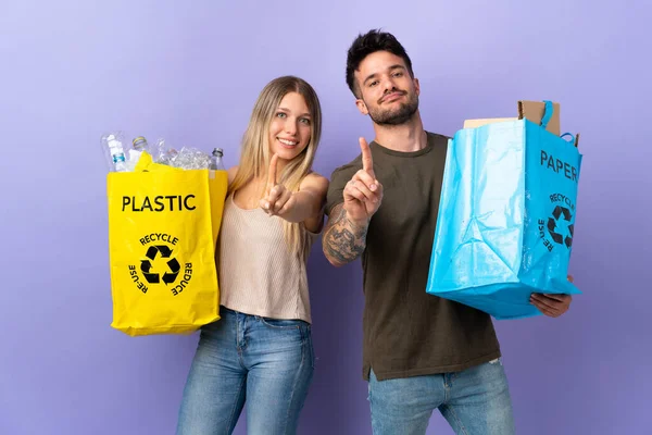 Reciclagem Jovem Casal Caucasiano Isolado Fundo Roxo Mostrando Levantando Dedo — Fotografia de Stock