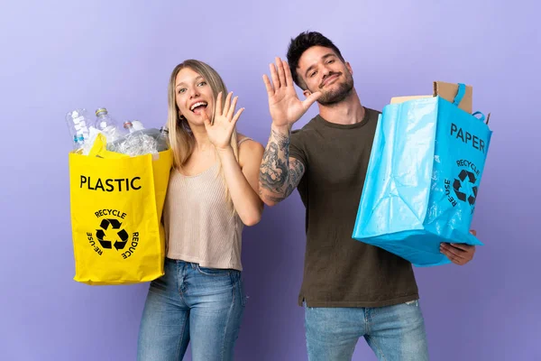 Joven Pareja Caucásica Reciclando Aislada Sobre Fondo Púrpura Saludando Con —  Fotos de Stock