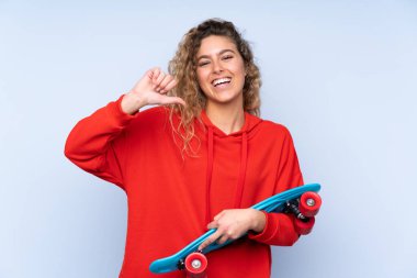 Mavi arka planda izole edilmiş kıvırcık saçlı, neşeli bir yüzü olan genç sarışın kadın.