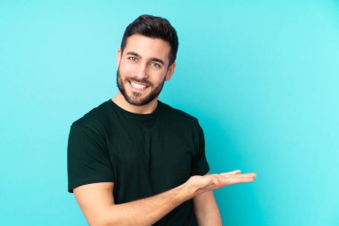 Kafkas yakışıklı adam mavi arka planda izole edilmiş bir fikir sunuyor ve gülümsüyor.
