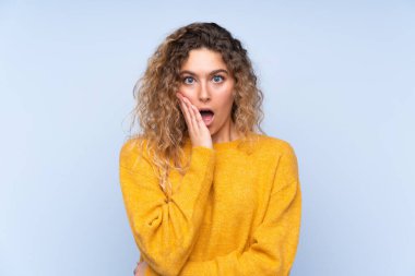 Mavi arka planda, kıvırcık saçlı genç sarışın kadın sağa bakarken şaşırmış ve şok olmuştu.