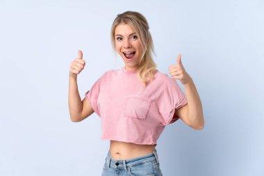 Sarışın kadın, izole edilmiş mavi arka planda baş parmak hareketi yapıyor.