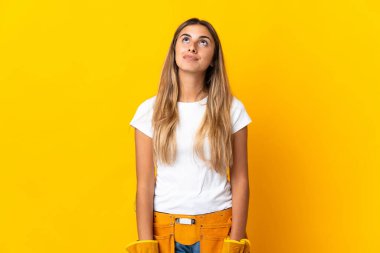 Genç İspanyol elektrikçi kadın izole edilmiş sarı duvardan yukarı bakıyor.