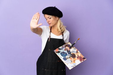 Mor arka planda izole edilmiş bir palet tutan genç Rus kadın dur hareketi yapıyor ve hayal kırıklığına uğruyor.