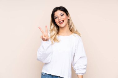 Bej arka planda izole edilmiş genç kız gülümsüyor ve zafer işareti gösteriyor.