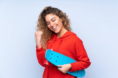 Mavi arka planda, kıvırcık saçlı, patenli genç sarışın kadın.