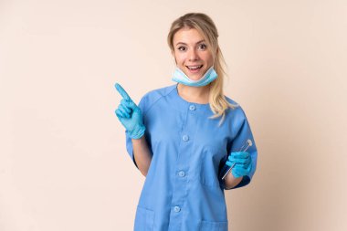 İzole edilmiş arka plan üzerinde aletleri tutan dişçi kadın parmak kenarı işaret ediyor