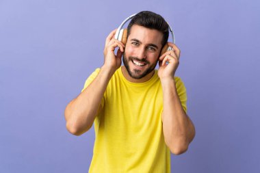 Mor arka planda izole edilmiş sakallı yakışıklı genç adam müzik dinliyor.
