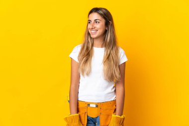 Genç İspanyol elektrikçi kadın, izole edilmiş sarı duvarın üzerinden bakıyor.