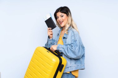 Gezgin genç elinde mavi arka planda izole edilmiş bir bavul, bavul ve pasaportla tatilde.