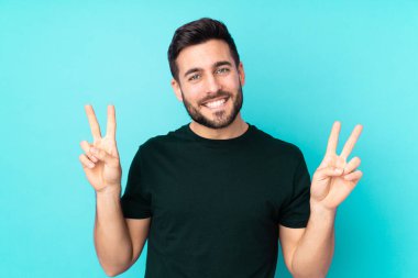Mavi arka planda izole edilmiş beyaz yakışıklı adam iki eliyle zafer işareti gösteriyor.