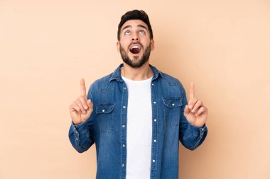 Beyaz tenli yakışıklı adam bej arka planda izole edilmiş şaşırmış ve yukarı bakıyor.
