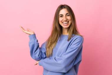 Soyutlanmış pembe arka planda genç bir kadın. Davet edilmek için ellerini yana uzatıyor.