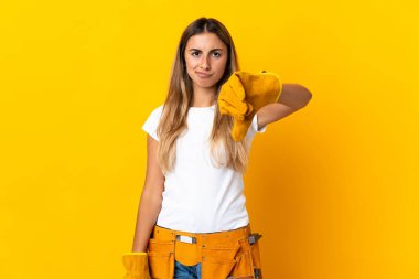 Genç İspanyol elektrikçi kadın, izole edilmiş sarı duvarın üzerinde negatif ifadeyle baş parmağını gösteriyor.