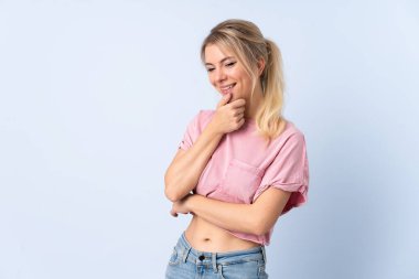 Sarışın kadın soyutlanmış mavi arka planda yan tarafa bakıyor ve gülümsüyor.