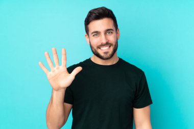 Beyaz tenli yakışıklı adam mavi arka planda izole edilmiş, parmaklarıyla beşi sayıyor.