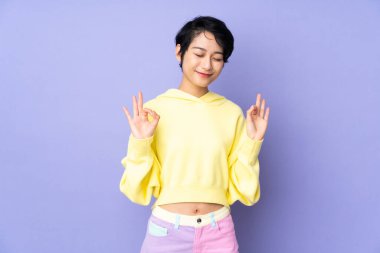 Genç Vietnamlı kadın, kısa saçlı, soyutlanmış mor arkaplanlı, zen pozlu.