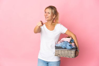 Elinde pembe arka planda izole edilmiş çamaşır sepeti tutan genç Rus kadın mutlu bir ifadeyle ön tarafı işaret ediyor.