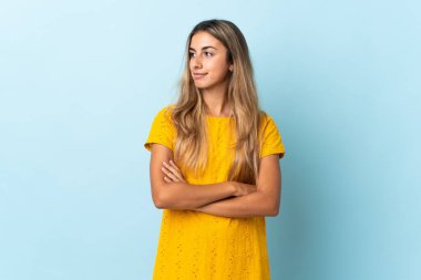 İzole edilmiş mavi arka planda genç İspanyol kadın yan tarafa bakıyor.
