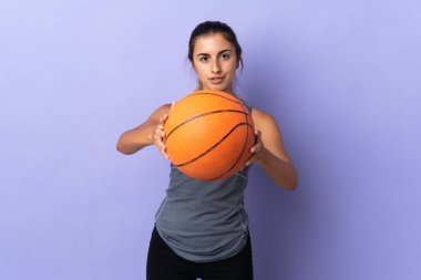 İzole edilmiş mor arka planda basketbol oynayan genç İspanyol kadın.