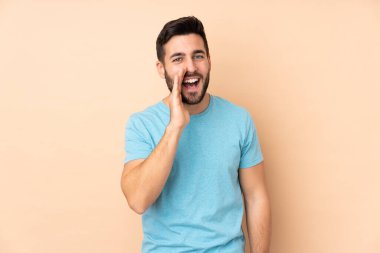 Beyaz tenli yakışıklı adam bej arka planda izole edilmiş ve ağzı açık bağırıyor.