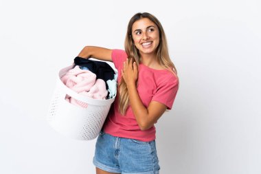 Beyaz arka planda izole edilmiş çamaşır sepetini tutan genç bir kadın gülümserken yukarı bakıyor.