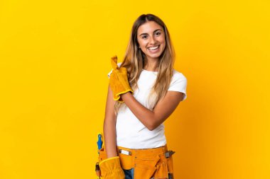 Genç İspanyol elektrikçi kadın, izole edilmiş sarı duvarın üzerinde bir ürün sunmak için yan tarafı işaret ediyor.