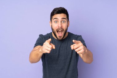 Kafkas yakışıklı adam şaşırdı ve izole edilmiş mor arka planda ön tarafı işaret etti.