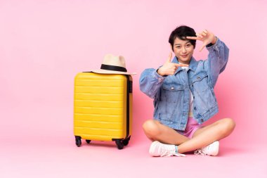 Genç gezgin Vietnamlı bir kadın bavuluyla yere oturmuş pembe arka planda izole bir şekilde yüzüne odaklanıyor. Çerçeve sembolü