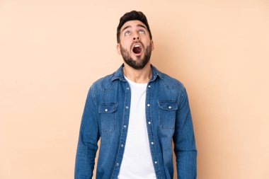 Beyaz tenli yakışıklı adam bej arka planda izole edilmiş yukarı bakıyor ve şaşırmış bir ifadeyle