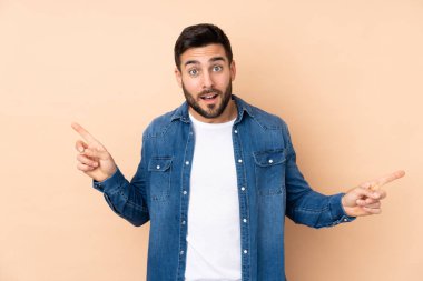 Beyaz tenli yakışıklı adam bej arka planda izole edilmiş, parmak uçlarında ve mutlu.