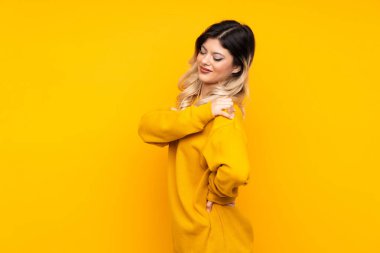 Sarı arka planda izole edilmiş genç bir kız omuz ağrısından muzdarip.