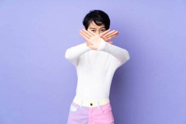 Mor arka planda kısa saçlı Vietnamlı genç bir kadın bir hareketi durdurmak için eliyle jest yapıyor.