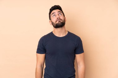 Beyaz tenli yakışıklı adam bej arka planda izole edilmiş ve yukarı bakıyor.