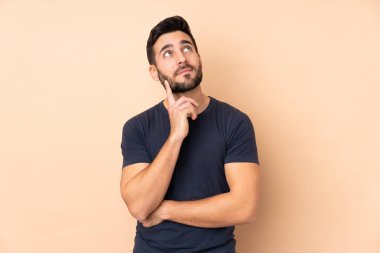 Beyaz tenli yakışıklı adam bej arka planda izole edilmiş, yukarı bakarken bir fikir düşünüyor.