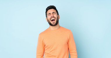 Kafkasyalı yakışıklı adam mavi arka planda gülüyor.