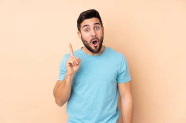 Beyaz tenli yakışıklı adam bej arka planda izole edilmiş. Çözümü bulmak için parmağını kaldırıyor.