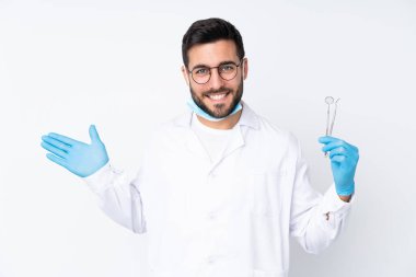 Beyaz arka planda izole edilmiş aletleri tutan dişçi adam davet etmek için ellerini yana uzatıyor