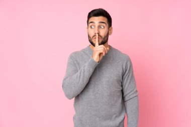 Kafkasyalı yakışıklı adam izole edilmiş arka planda sessizlik işareti gösteriyor. Parmağını ağzına sokuyor.