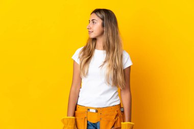 Genç İspanyol elektrikçi kadın, yalıtılmış sarı duvarın üzerinden yan tarafa bakıyor.