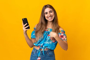 İzole edilmiş sarı arka planda cep telefonu kullanan genç bir kadın.